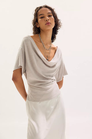 Woman wearing a light gray top and white pants on a plain background