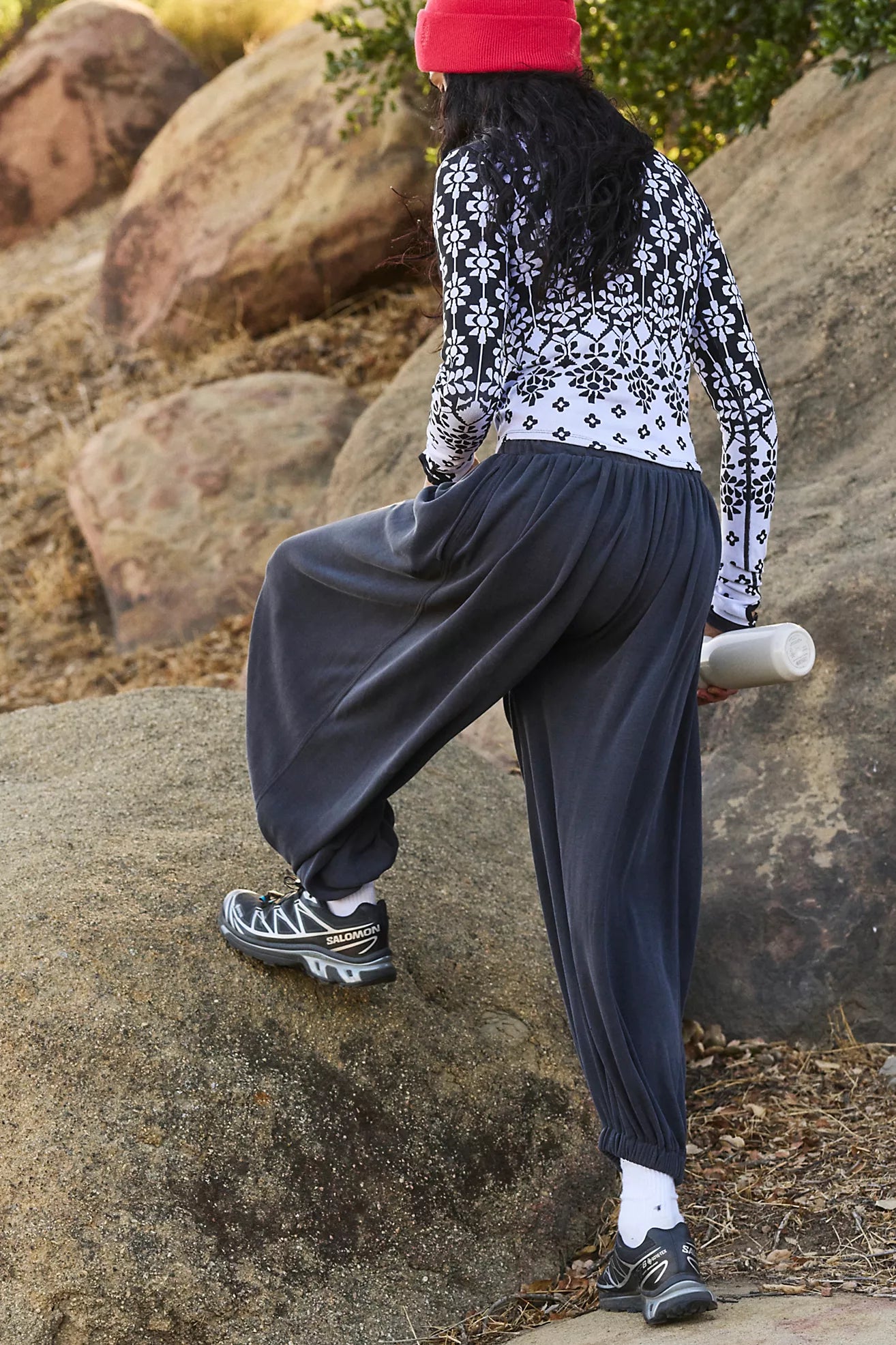 Person wearing a patterned shirt and dark pants sitting on rocks outdoors.