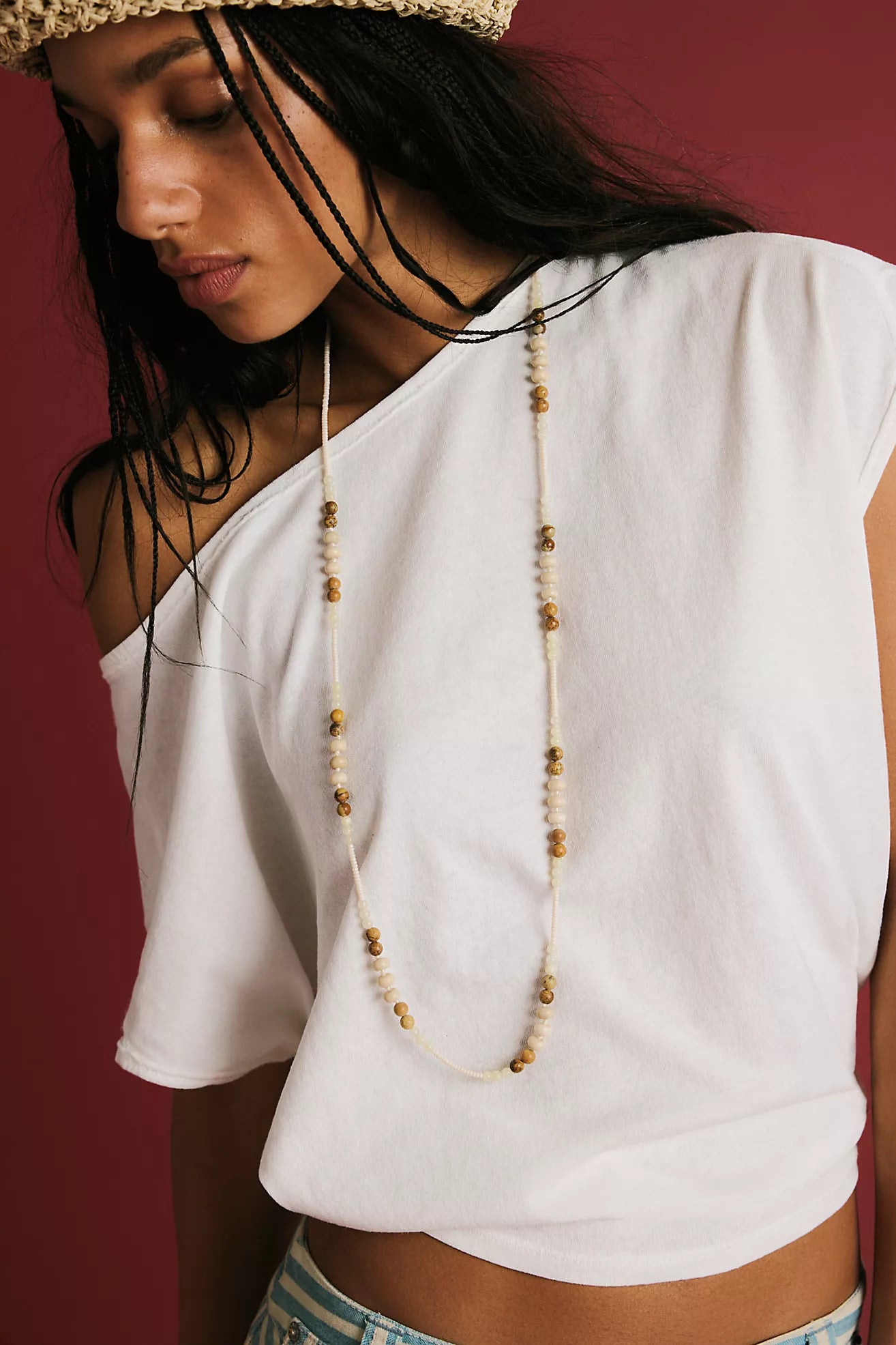 Woman wearing a white top and a long necklace with a red background