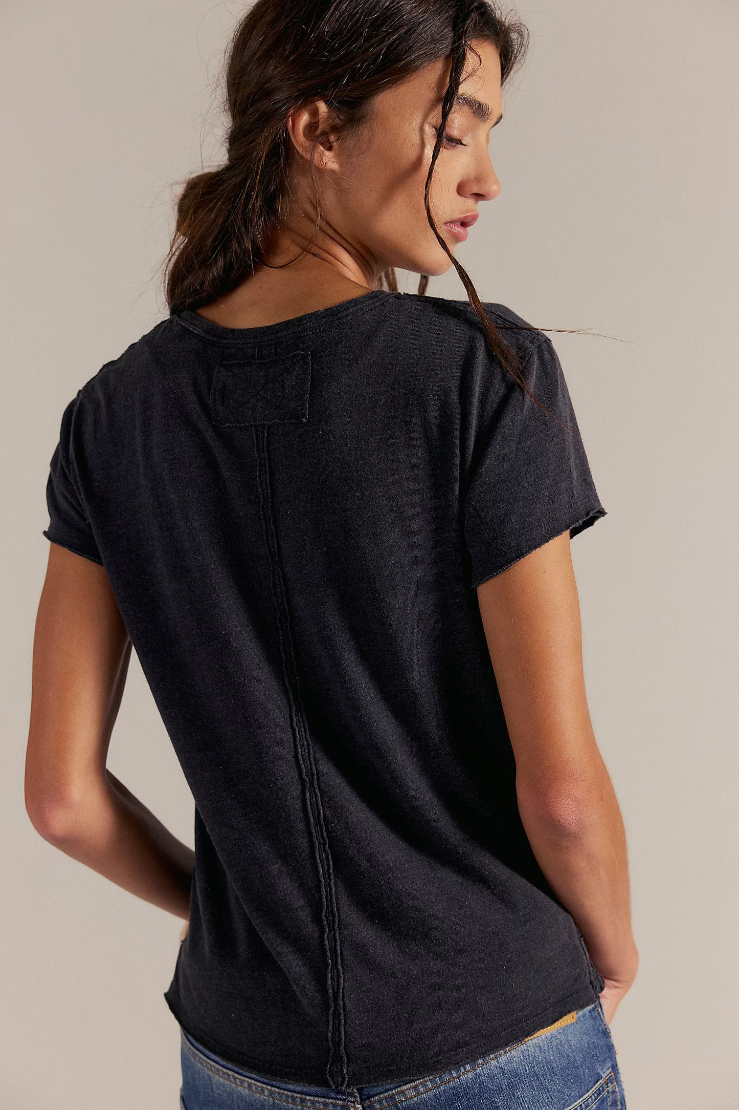Woman wearing a black t-shirt and blue jeans against a plain background