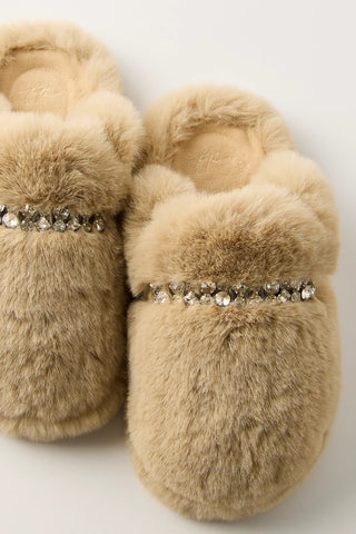 A pair of beige faux fur slip-on slippers decorated with a horizontal row of clear rhinestones across the top, shown against a plain light background.