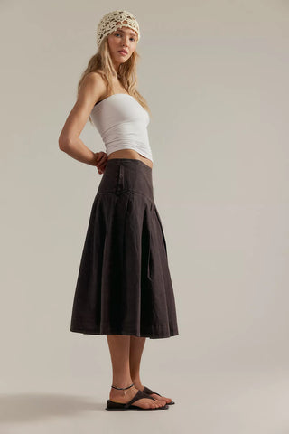 Woman wearing a white top and brown skirt against a plain background
