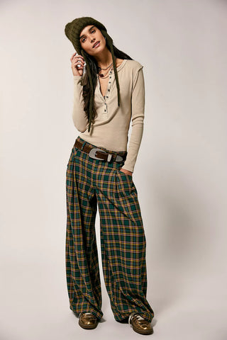 Woman wearing a beige top and plaid pants with a green hat on a plain background
