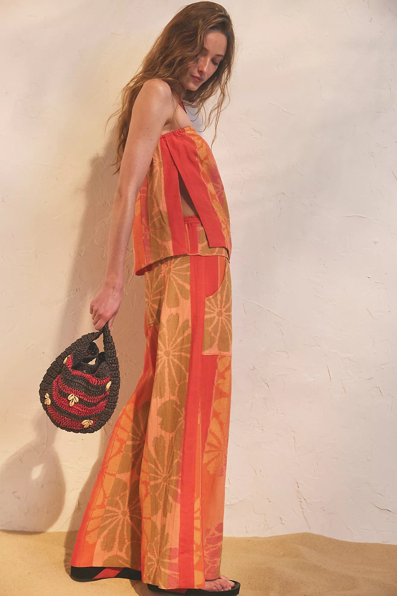 Woman wearing a colorful outfit with a patterned bag against a plain background
