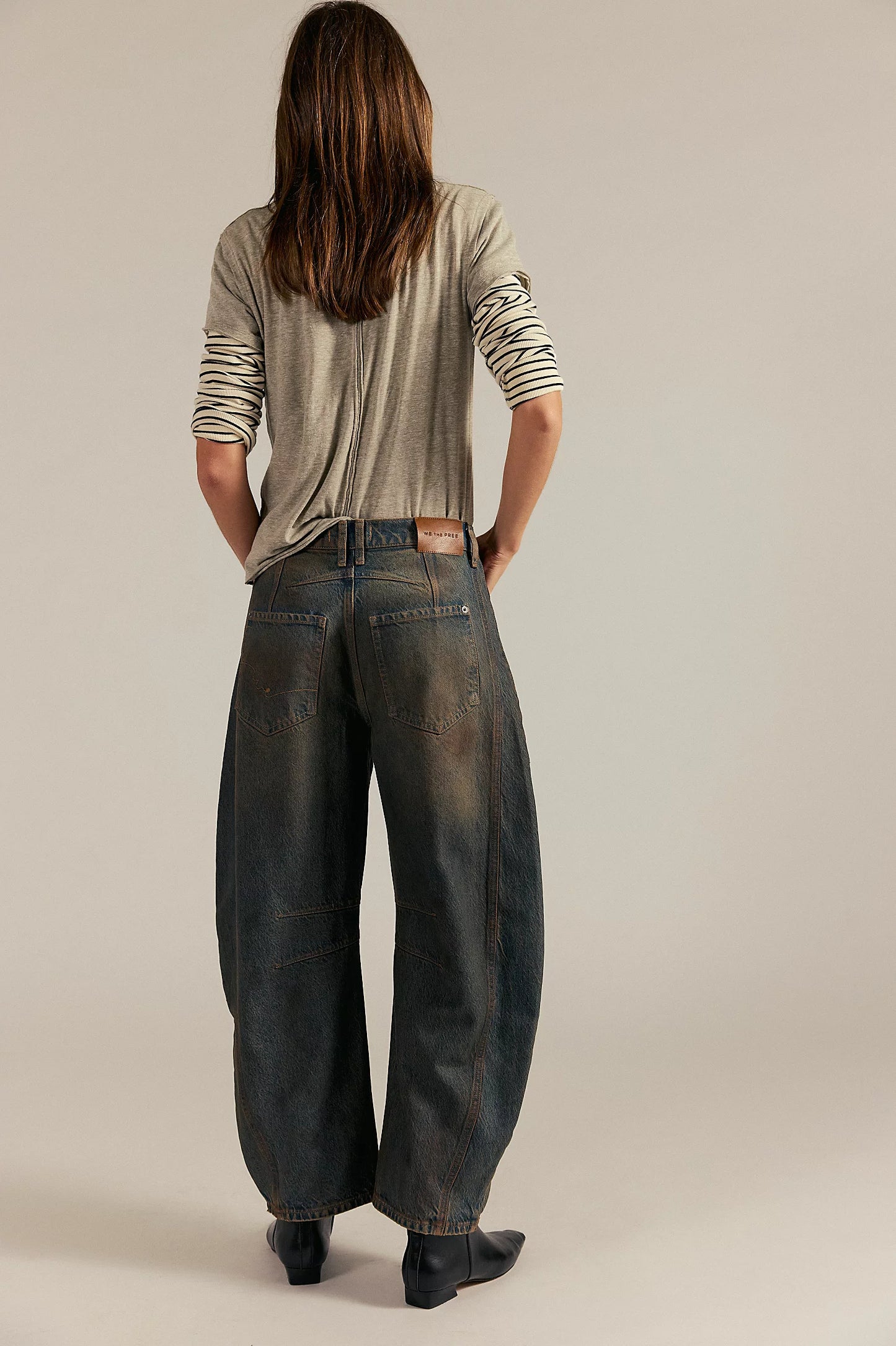 Person wearing a light gray long-sleeve shirt and dark blue jeans on a beige background