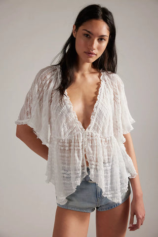 Woman wearing a white lace top and denim shorts on a plain background
