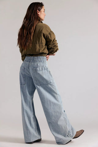 Person wearing a green jacket and light blue jeans on a plain background