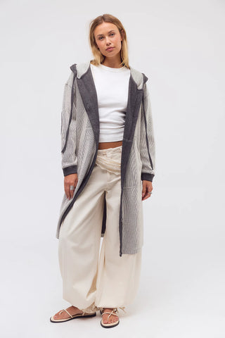 Woman wearing a long gray cardigan over a white top and beige pants on a white background