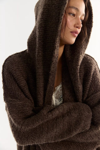 Women wearing a brown knit cardigan and cream jeans in front of a neutral photo background.