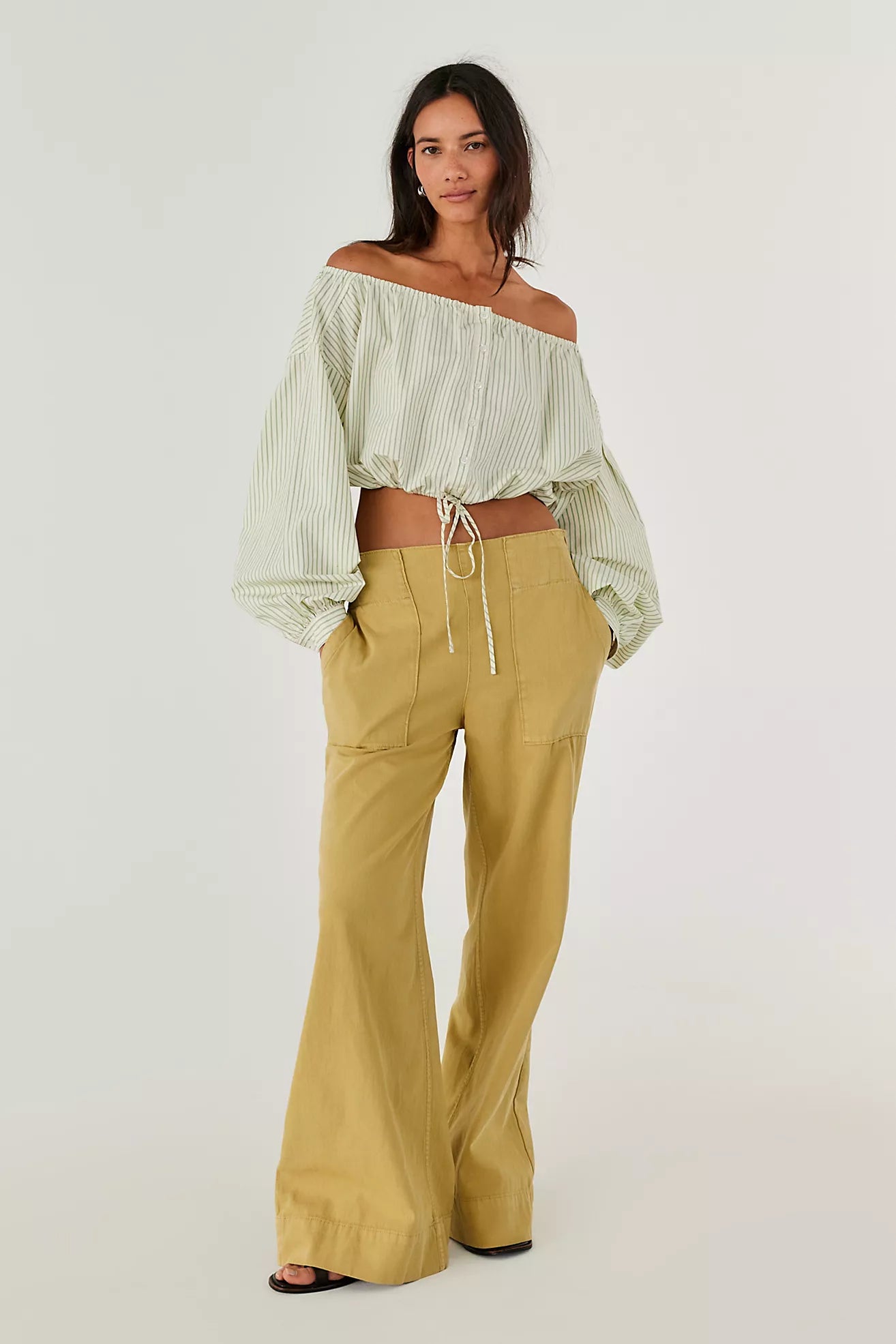 Woman wearing a light green off-shoulder top and mustard yellow pants on a white background