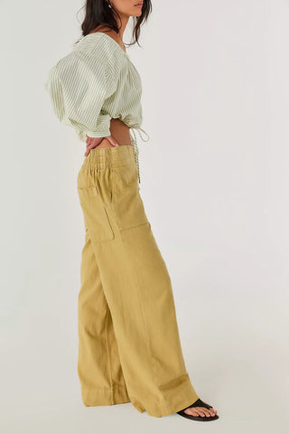 Person wearing a green striped top and mustard yellow wide-leg pants on a white background