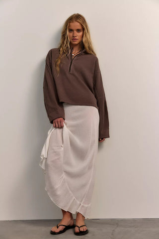 Woman wearing a brown top and white skirt against a plain wall
