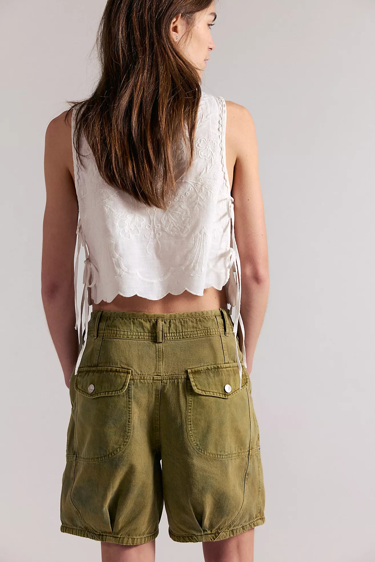 Woman wearing a white sleeveless top and green shorts on a plain background