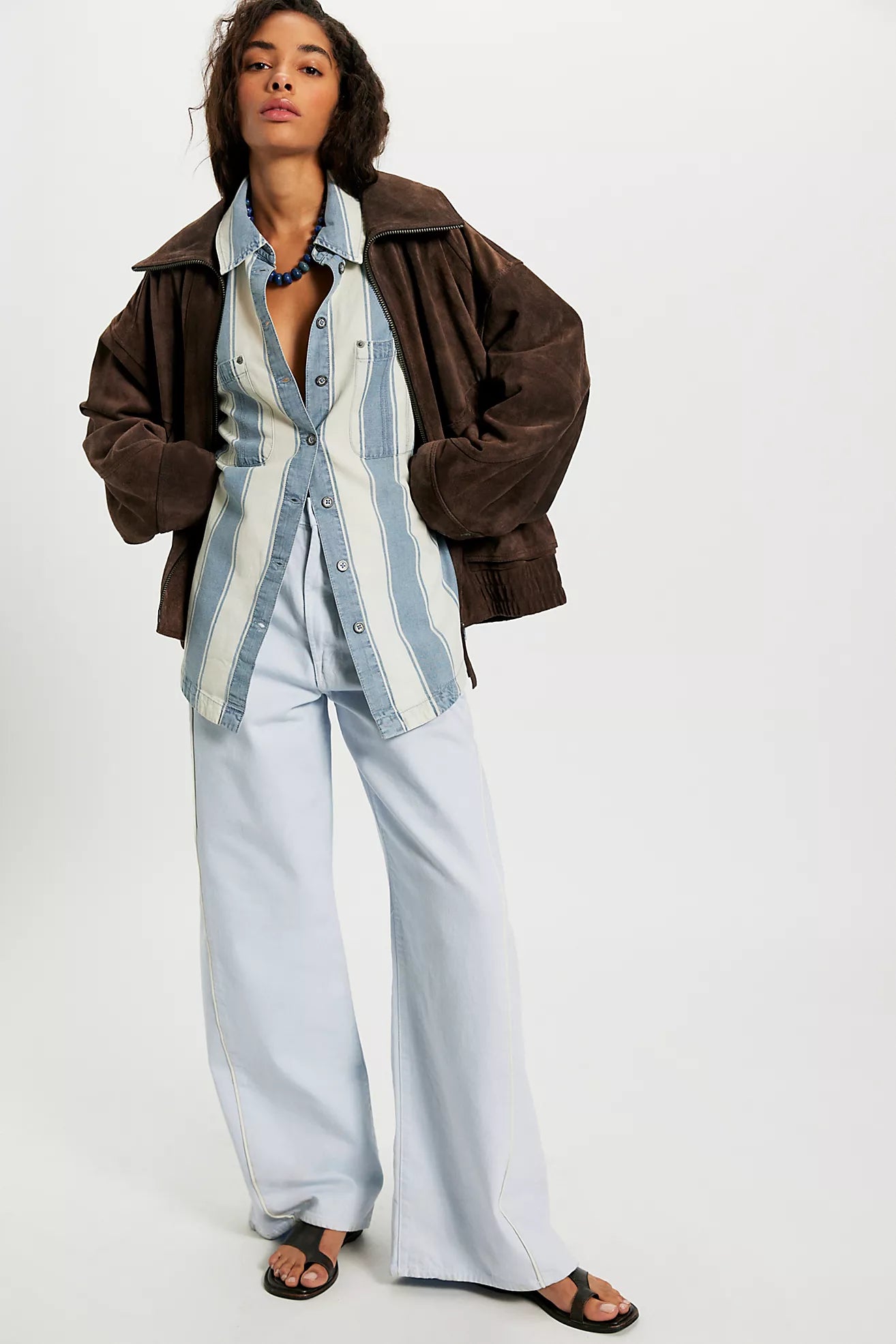 Person wearing a brown jacket, striped shirt, and light blue pants on a white background
