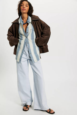 Person wearing a brown jacket, striped shirt, and light blue pants on a white background