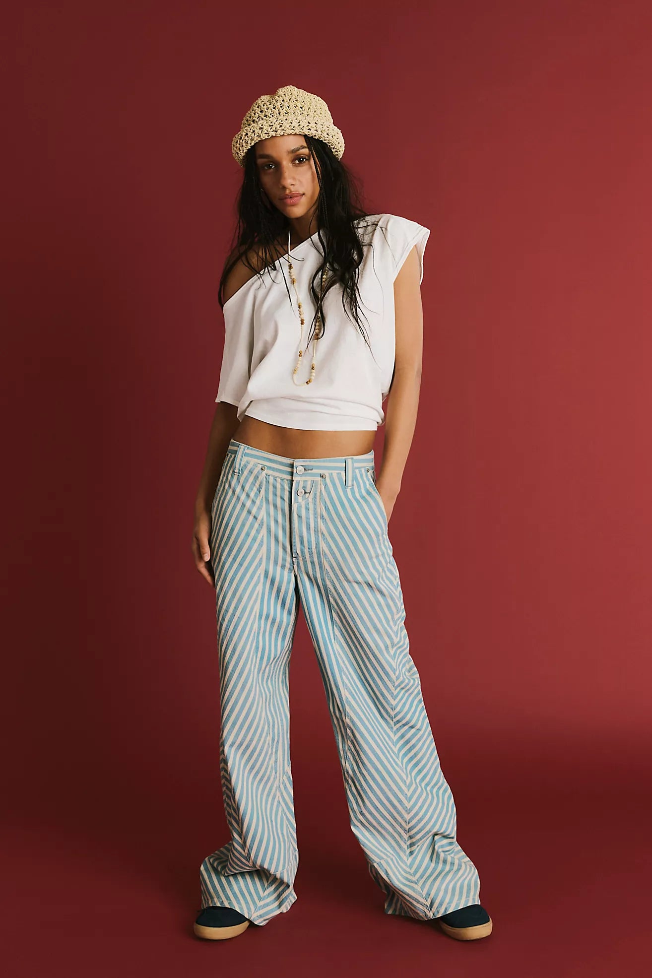 Woman wearing a white off-shoulder top and striped pants against a red background