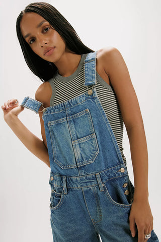 Person wearing denim overalls with a striped tank top on a white background