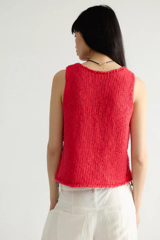 A woman shown from the back wearing a bright red sleeveless knit top and white pants against a plain light background.