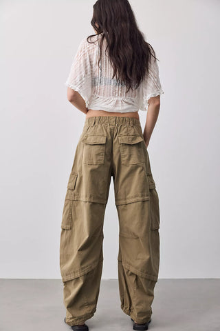 A model shown from the back wearing wide-leg olive cargo pants and a white textured short-sleeve crop top against a plain light gray studio background.