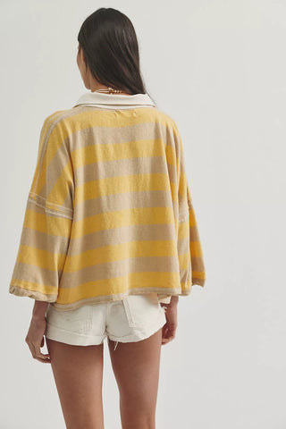 Person wearing a yellow and beige striped shirt with white shorts on a plain background