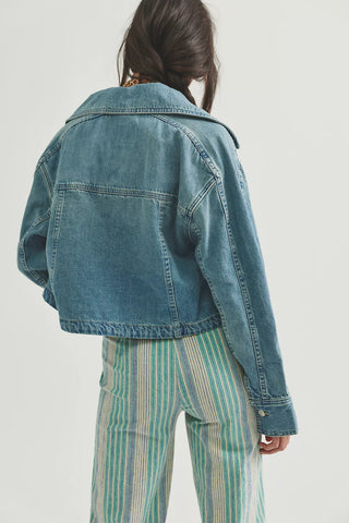 Person wearing a blue denim jacket and striped pants on a light gray background