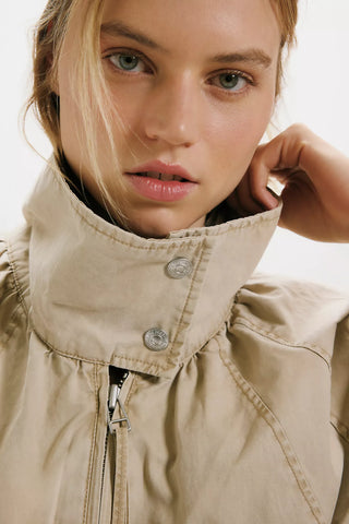 Close-up of a person wearing a beige jacket with a neutral background