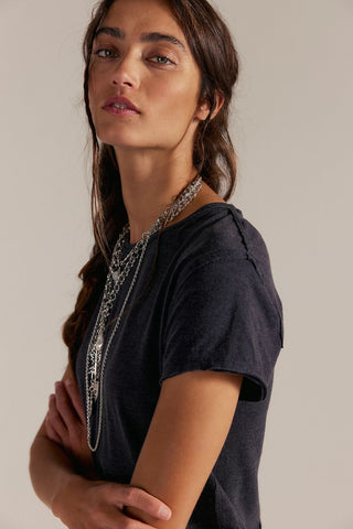Woman wearing a black t-shirt with a long necklace against a neutral background