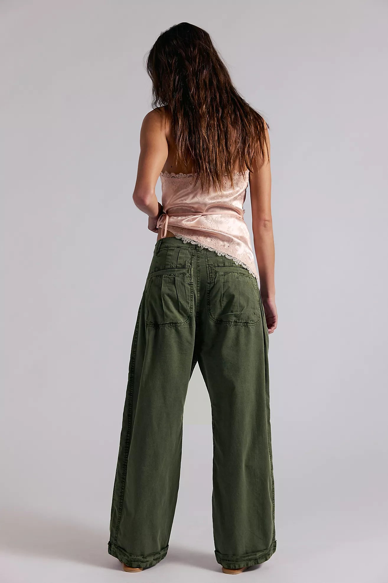 Person wearing green wide-leg pants and a pink top on a plain background