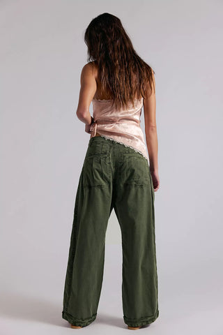 Person wearing green wide-leg pants and a pink top on a plain background