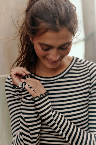 Woman wearing a black and white striped shirt, smiling and holding a small object.