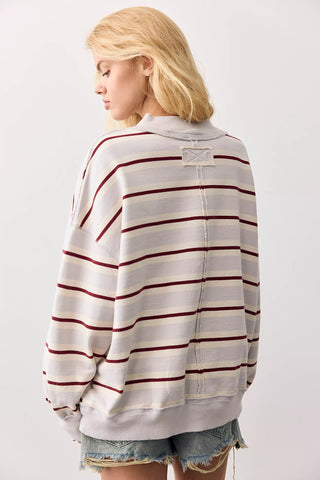 A woman shown from the back wearing a light gray oversized sweatshirt with thin dark red horizontal stripes and frayed denim shorts against a plain light background.