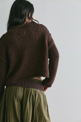 A person shown from the back wearing a dark brown ribbed knit cropped sweater and an olive green skirt against a plain light gray background.