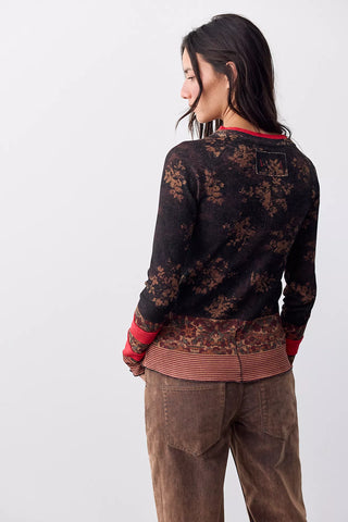 A woman shown from the back wearing a dark brown and black floral knit sweater with red ribbed trim, paired with brown corduroy pants, against a plain white studio background.