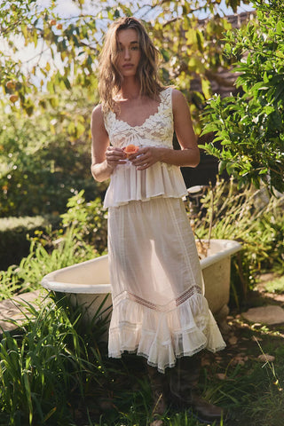 Woman in a white dress standing in a garden with a bathtub.