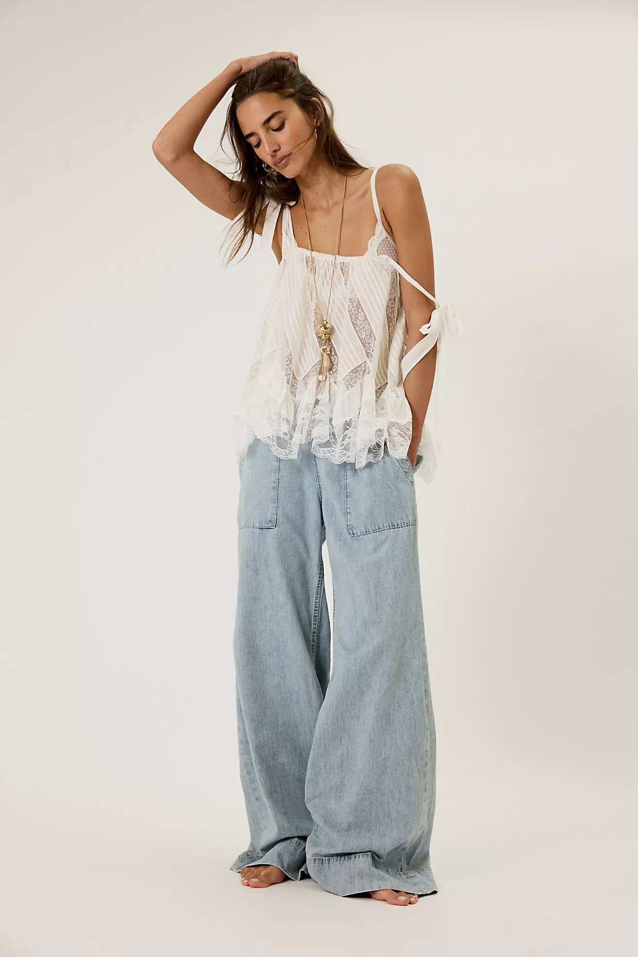 Woman wearing a white lace top and light blue jeans against a plain background