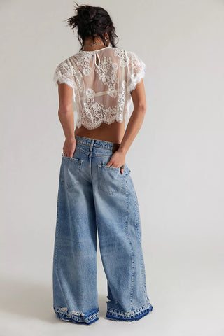 Person wearing a lace top and wide-leg jeans on a plain background