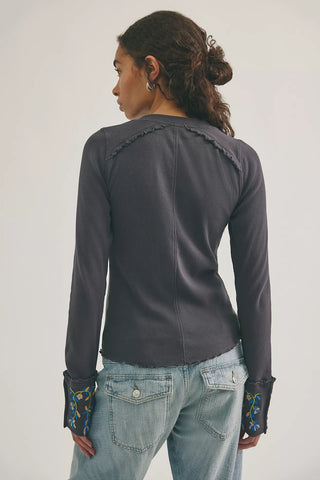 Person wearing a dark gray long-sleeve top with floral cuffs on a white background