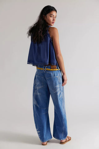 Woman wearing a blue denim top and wide-leg jeans on a plain background