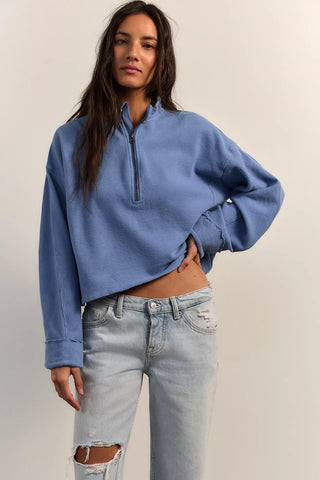 Woman wearing a blue cropped sweater and light blue jeans against a plain background