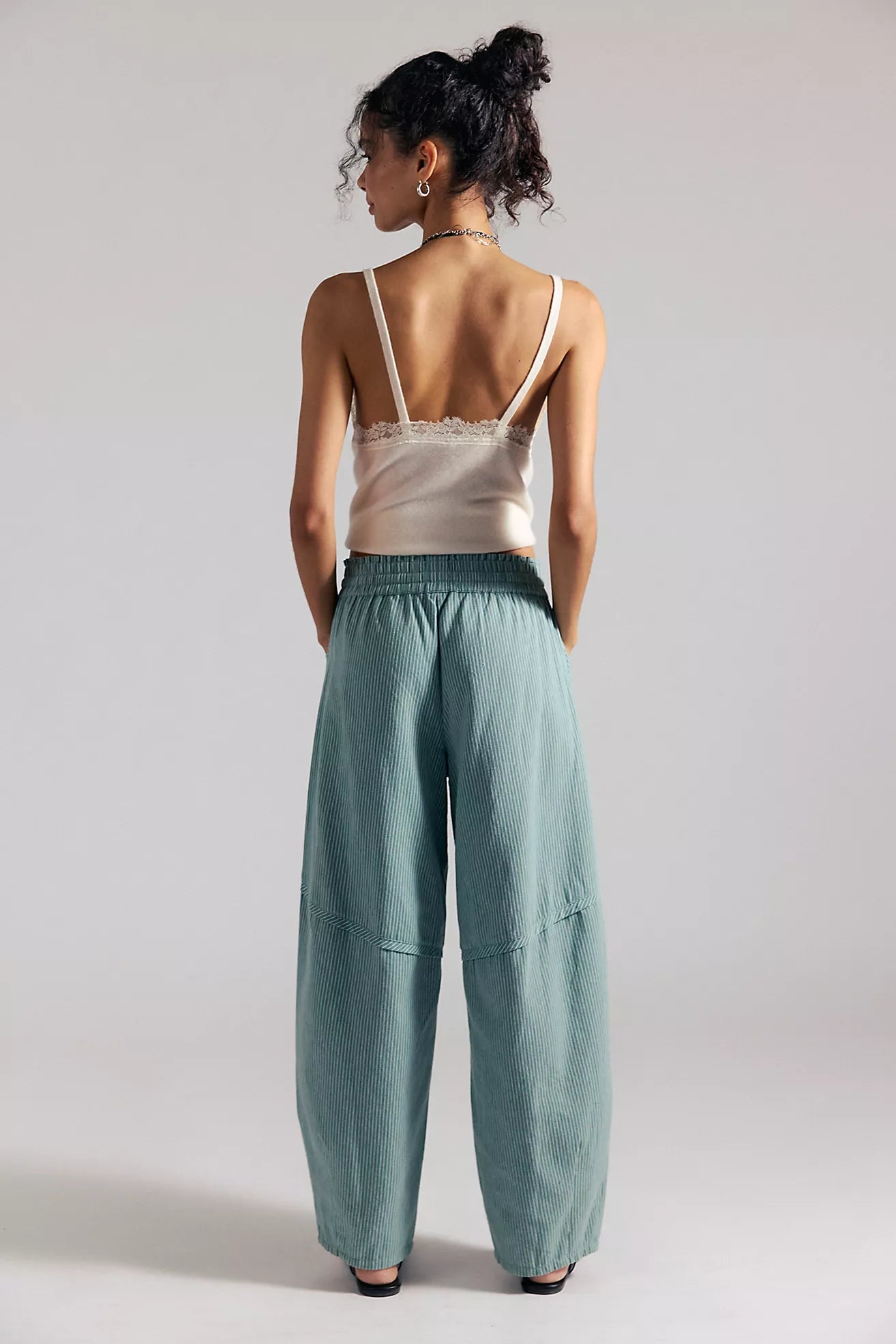 Woman wearing a white top and teal pants against a plain background