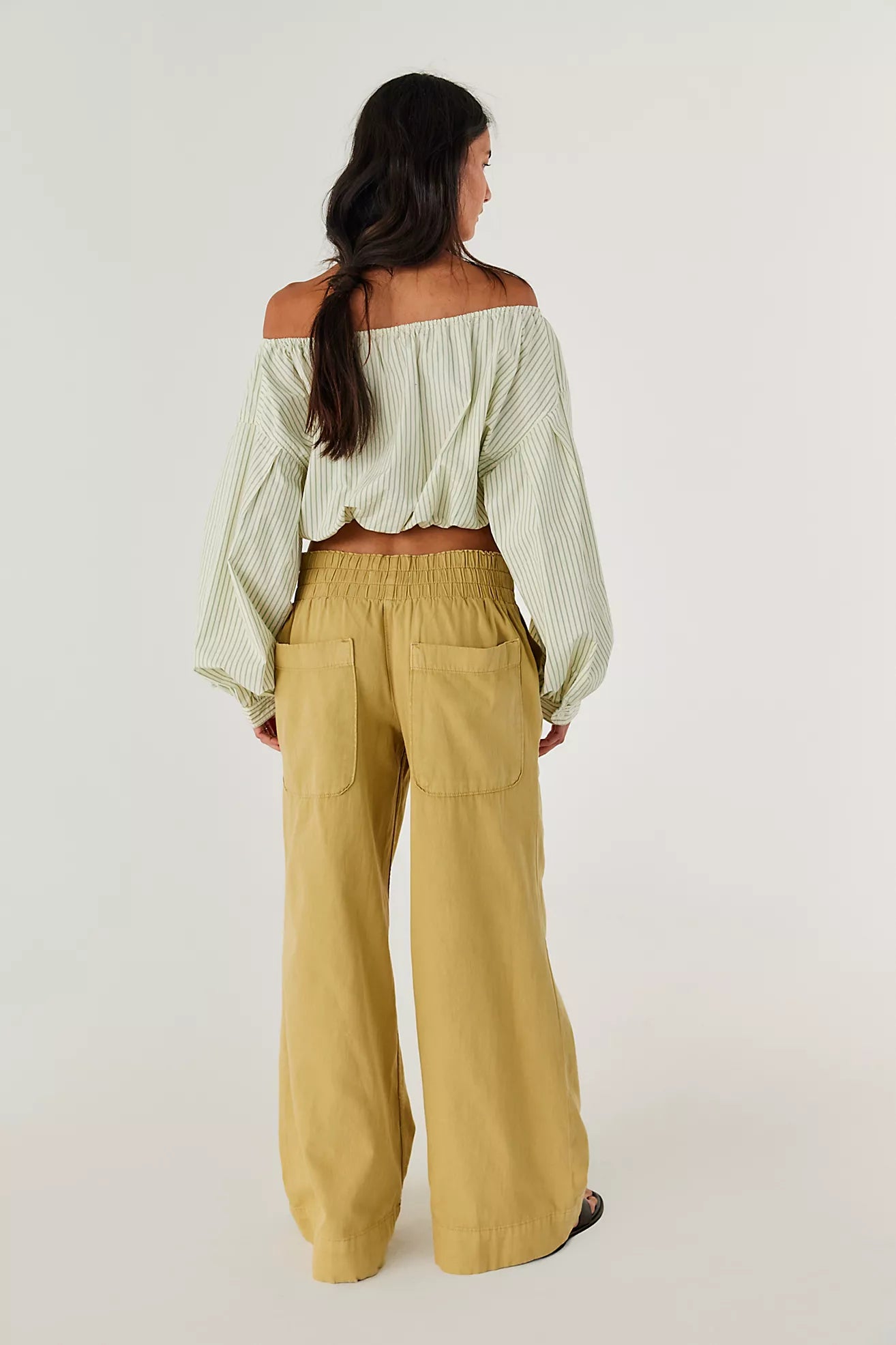 Woman wearing a light green off-shoulder top and mustard yellow wide-leg pants on a white background