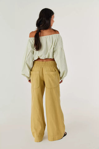 Woman wearing a light green off-shoulder top and mustard yellow wide-leg pants on a white background