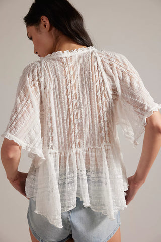 Woman wearing a white lace top and denim shorts against a plain background