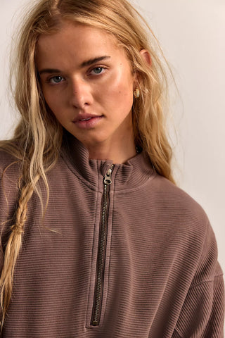 Woman wearing a brown zip-up sweatshirt against a plain background