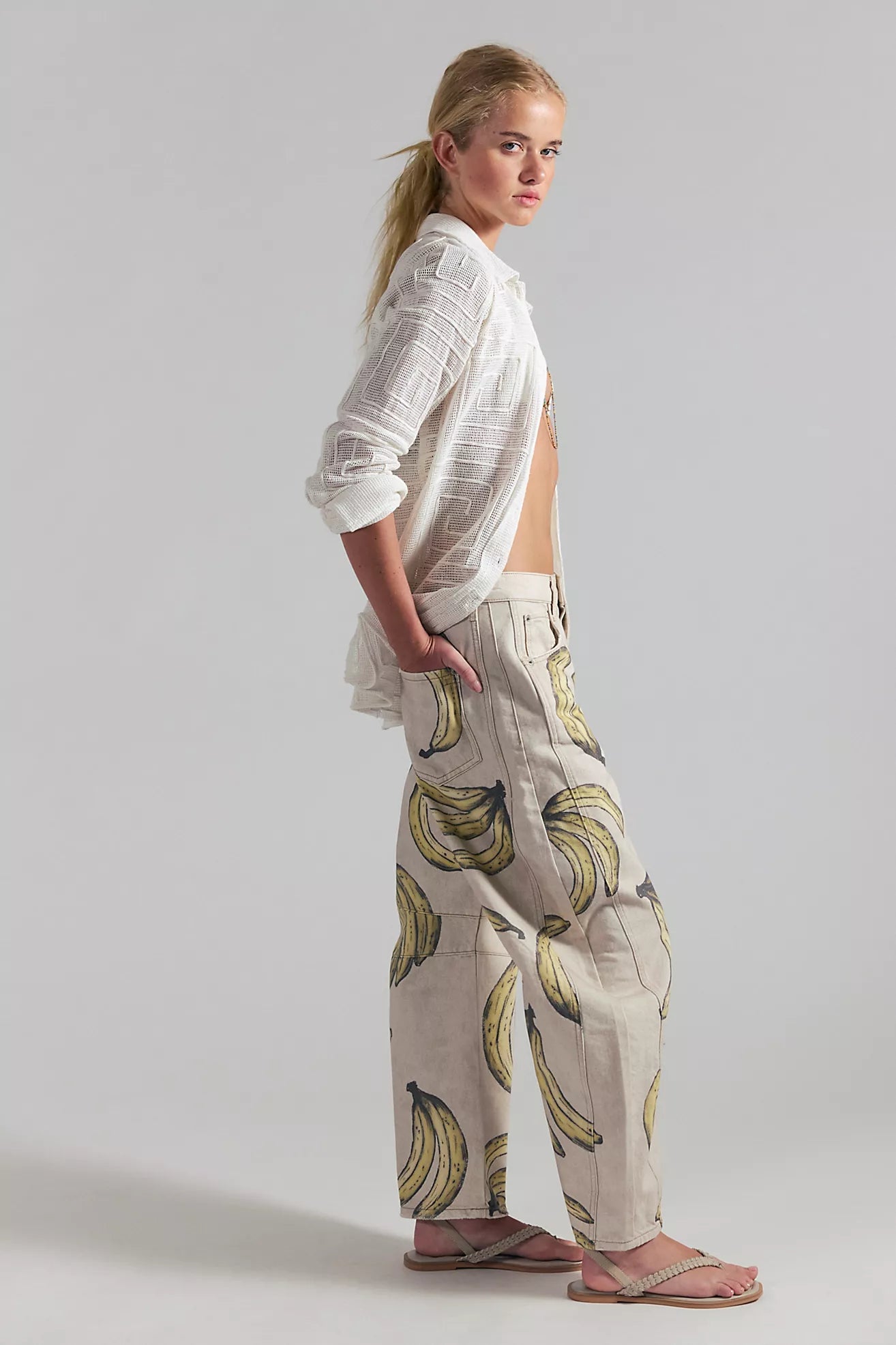 Woman wearing a white shirt and banana-patterned pants on a plain background