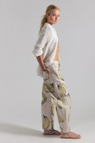 Woman wearing a white shirt and banana-patterned pants on a plain background