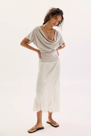 Woman wearing a light gray top and white skirt with lace details on a white background