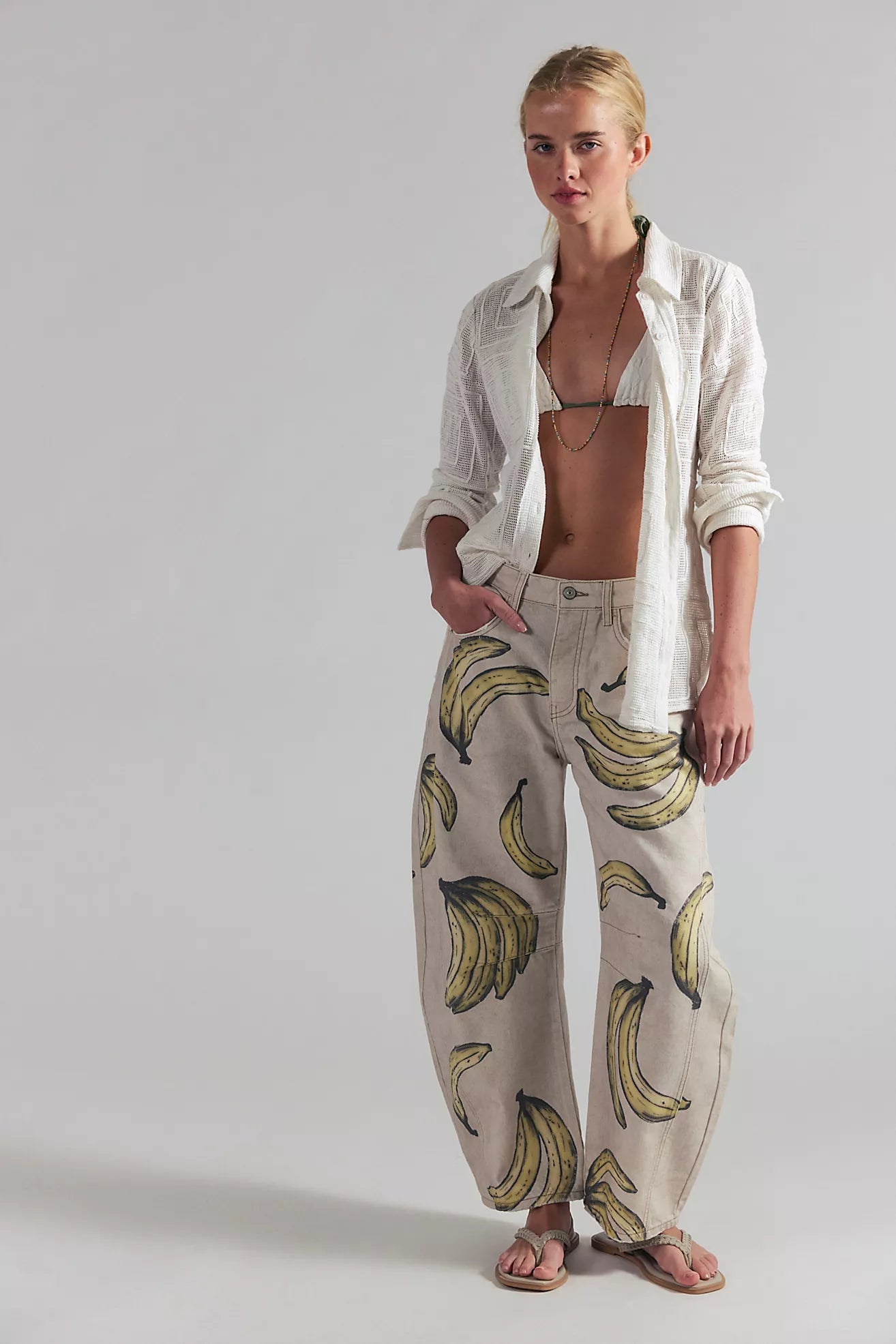 Woman wearing a white shirt and banana-patterned pants on a plain background