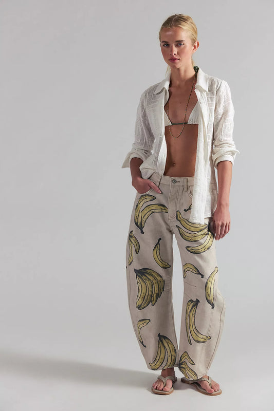 Woman wearing a white shirt and banana-patterned pants on a plain background