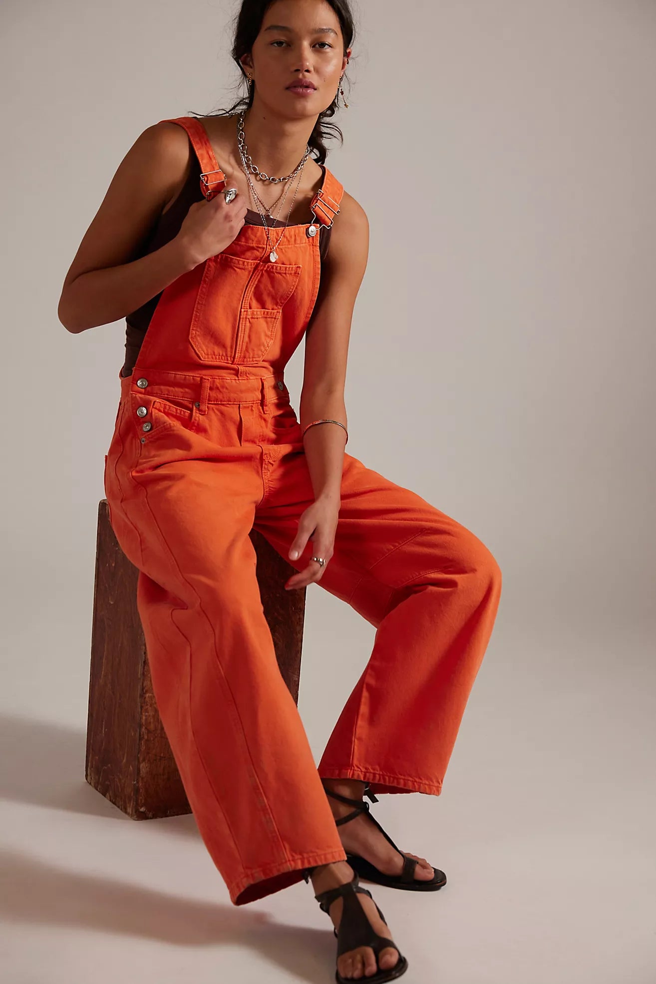 Person wearing an orange jumpsuit sitting on a wooden block against a plain background